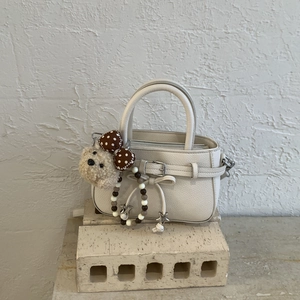 Close-up of beige lychee leather bag with decorative bow and plush bear charm