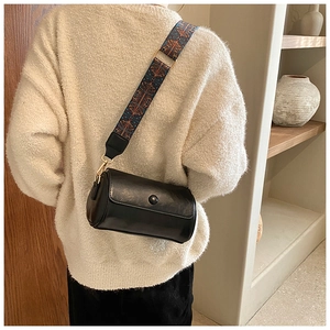 Elegante borsa a bauletto nera con tracolla geometrica in un ambiente interno accogliente