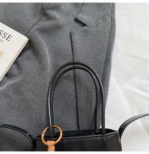 Detail of black matte bucket bag with cylindrical handles and gold metal charm accessory