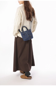 Detail of dark blue denim mini shoulder bag with metal buttons and two front flap pockets