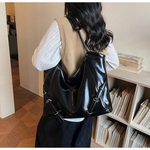 Détail d'un grand cabas noir brillant avec boucles métalliques sur fond de bibliothèque