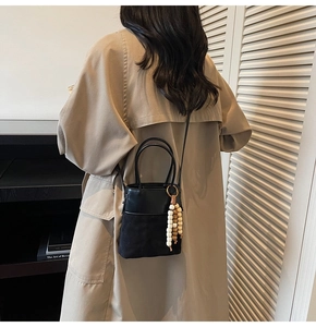 Detail of black suede bucket bag with multi-color wooden bead tassel and elegant leather strap