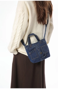 Detail of dark blue denim crossbody bag with contrast stitching and metal button