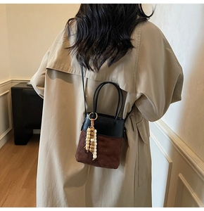 Detail of suede bucket bag with wooden bead charm and long black shoulder strap