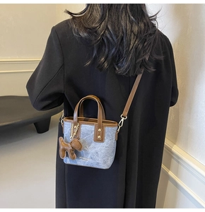 Dettaglio di una borsa a secchiello in denim con finiture in pelle marrone su modella