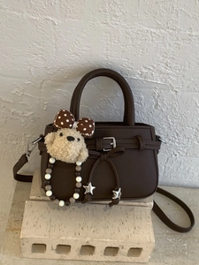 Deep brown leather handbag with luxury pebble texture and plush dog charm on stone base