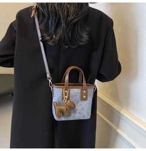 Dettaglio borsa a secchiello in denim blu con manico in pelle marrone e ciondolo cane