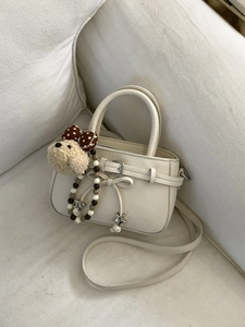 Chic beige mini crossbody bag with star pendant and plush bear charm on white sofa