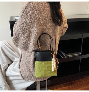 Detail of a two-tone bucket bag with green suede lozenge pattern and wooden bead charm