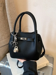 Chic black litchi grain bucket bag with silver lock and decorative pendant on travel luggage