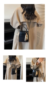 Close-up of black bucket bag with mixed textures, suede paneling, and wooden bead tassel