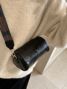Borsa a cilindro retrò nera con ampia tracolla geometrica indossata da una modella