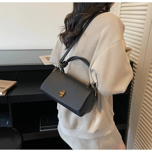 Detail shot of black pebbled leather handbag with golden metal turn-lock and handle