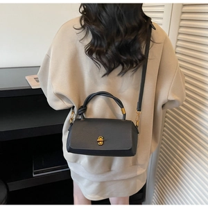 Rear view of a model wearing a black pebbled leather handbag with a gold twist lock
