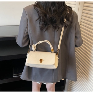 Model wearing a cream leather crossbody bag with knot handle and gold hardware detail