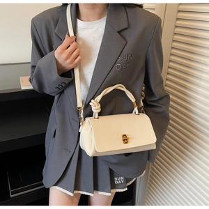 Detail of cream lychee texture handbag featuring a unique rope knot handle and metal lock