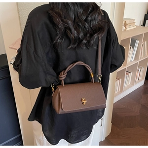 Close-up of brown litchi pattern leather handbag with unique knotted handle and gold twist lock
