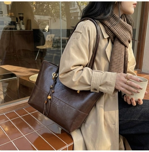 Detail of vintage brown leather tote bag with wooden bead charm and fringe tassel
