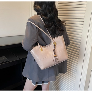 Chic beige leather tote bag with elegant wood bead tassel shown on model's shoulder