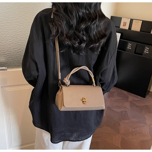 Beige pebble leather handbag with knot handle shown on a model in a minimal room