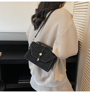 Detail view of a black suede-textured crossbody bag with white stitching and gold hardware