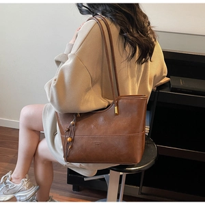 Brown leather tote bag detail with bead charm and debossed fashion logo on surface