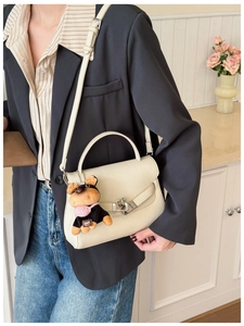 Close-up of litchi grain beige leather handbag with silver clasp and plush dog pendant