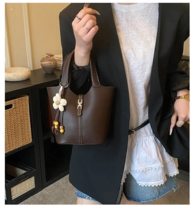 Detail of dark brown pebble leather bucket bag with metal H-buckle and floral charm