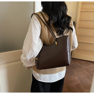 Deep brown leather tote bag with gold metal hardware and smooth finish on a shoulder model