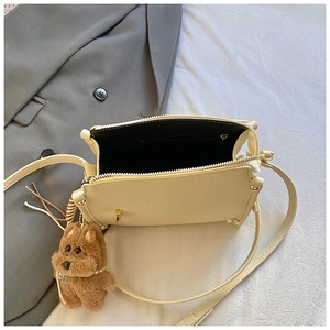 Detail view of cream pebble leather crossbody bag with top zipper and plush puppy charm