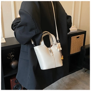 Detail of ivory lychee leather bucket bag with silver clasp and floral charm on a model