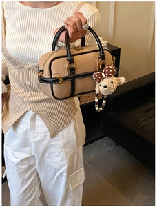 Détail du sac à main beige en cuir grainé avec bordure noire et breloque ours en peluche