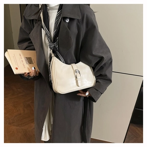 Detail of a creamy white leather crescent bag with silver metallic buckle on shoulder
