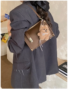 Close-up of dark brown leather handbag with lychee texture and cute teddy bear charm