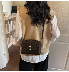 Detail of dark brown matte crossbody bag with metal buckle and top handle shown on model
