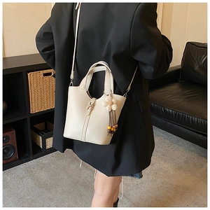 Detail showing creamy white lychee grain leather bucket bag with a floral charm