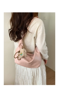 Side view of a pink crescent shoulder bag with a cute lamb charm on a minimalist model