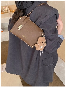 Close-up of brown leather bag with gold buckle, logo detail and cute bear pendant