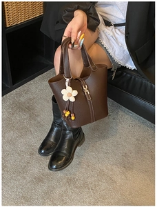 Detail of a brown leather bucket bag featuring a white flower charm and buckle strap