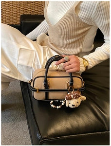 Détail du sac baguette bicolore avec charm chien en peluche sur un canapé en cuir