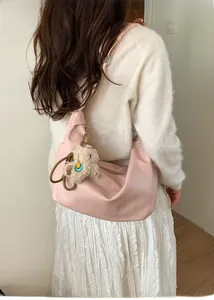Detailed back view of a light pink crescent dumpling bag worn by a model with a bear charm