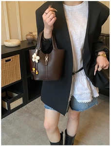 Detail of dark brown lychee leather bucket bag with metal lock and floral charm