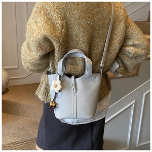 Detailed close-up of a grey lychee-grain leather bucket bag with floral pendant