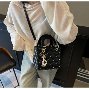 Détail d'un sac à main noir matelassé cœur avec nœud en perles et métal doré