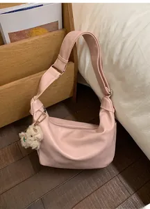 Pink hobo bag detail with plush charm on wooden floor and soft bedding background
