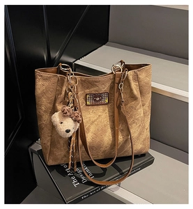 Detail of brown tote bag with embossed bear patterns and plush bear keychain accessory