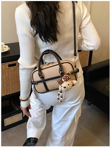Détail du sac boston en cuir beige avec breloque ours et bordures noires contrastées