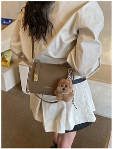 Close-up of brown leather square crossbody bag with gold buckle and plush dog charm