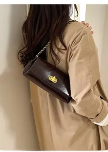 Detail of dark brown leather shoulder bag with gold chain strap and turn-lock closure