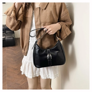 Close-up of black retro underarm bag with silver buckle worn by a model in casual style